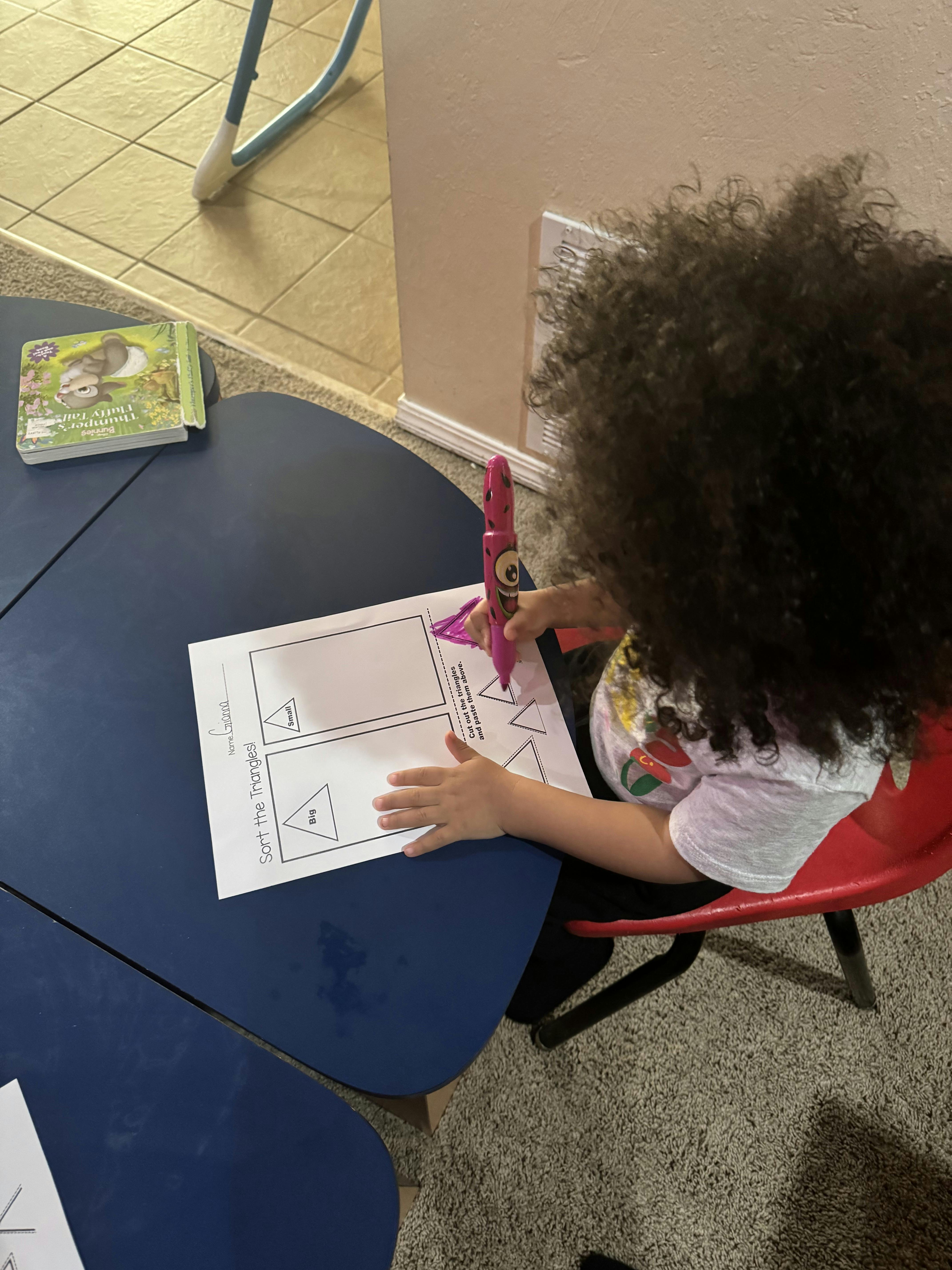 Child coloring in triangles on a worksheet titled "Sort the Triangles!"