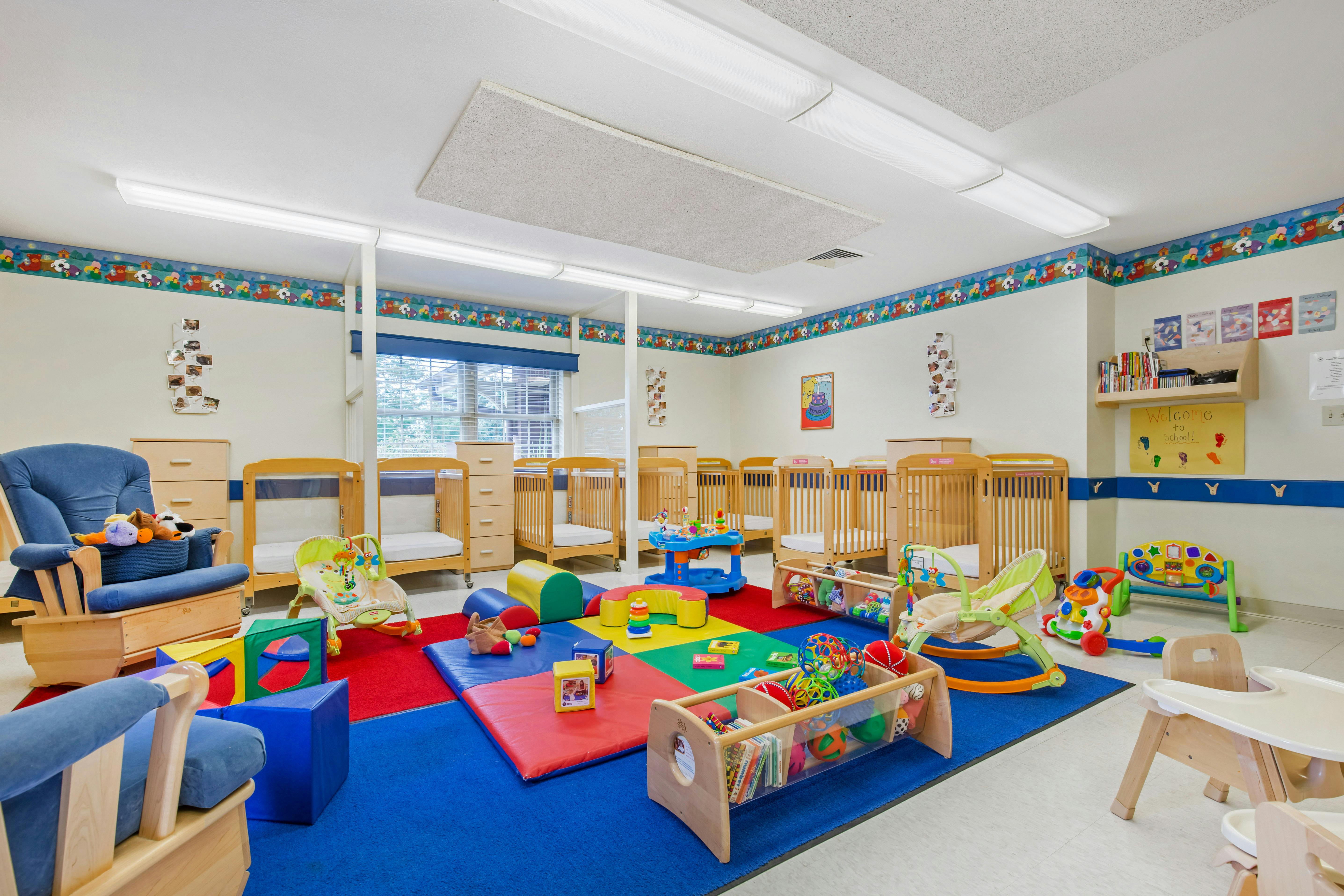 A colorful playroom with multiple cribs, a blue rocking chair, and play mats
