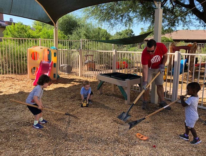 Adult and children raking and shoveling wood chips in a playground