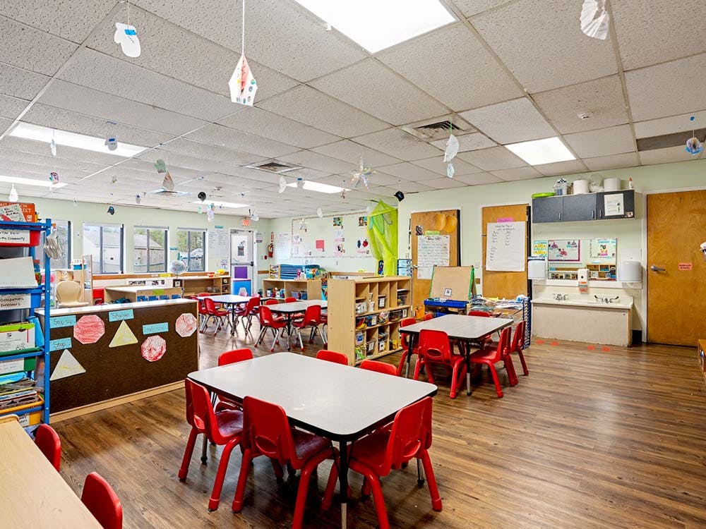 Classroom with small tables and chairs, artwork on walls, and decorations hanging from the ceiling