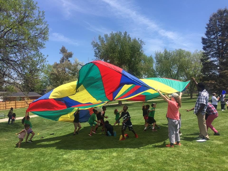 People and children playing with a large colorful parachute on a grassy field