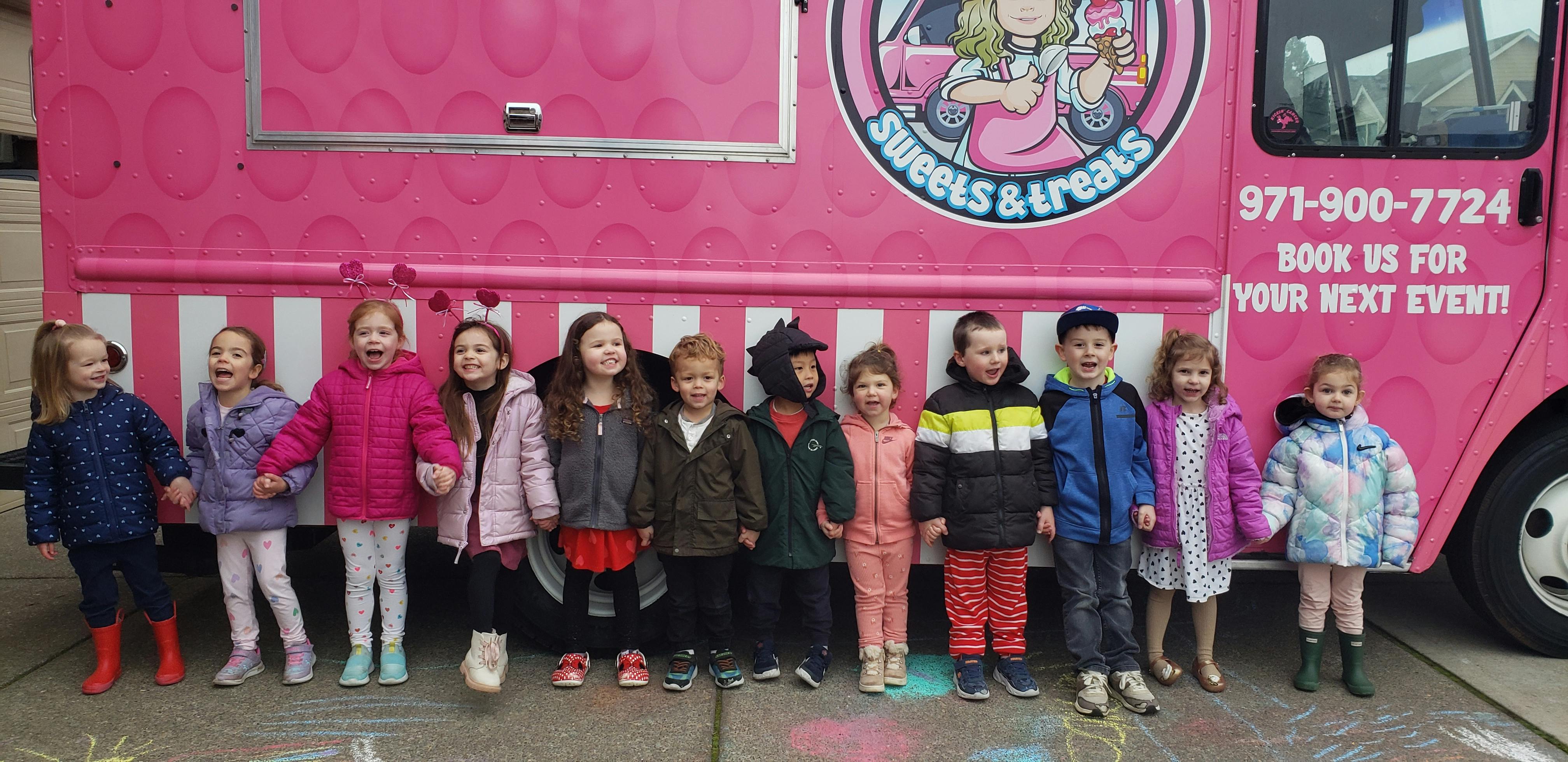 Children standing in a line in front of a pink food truck