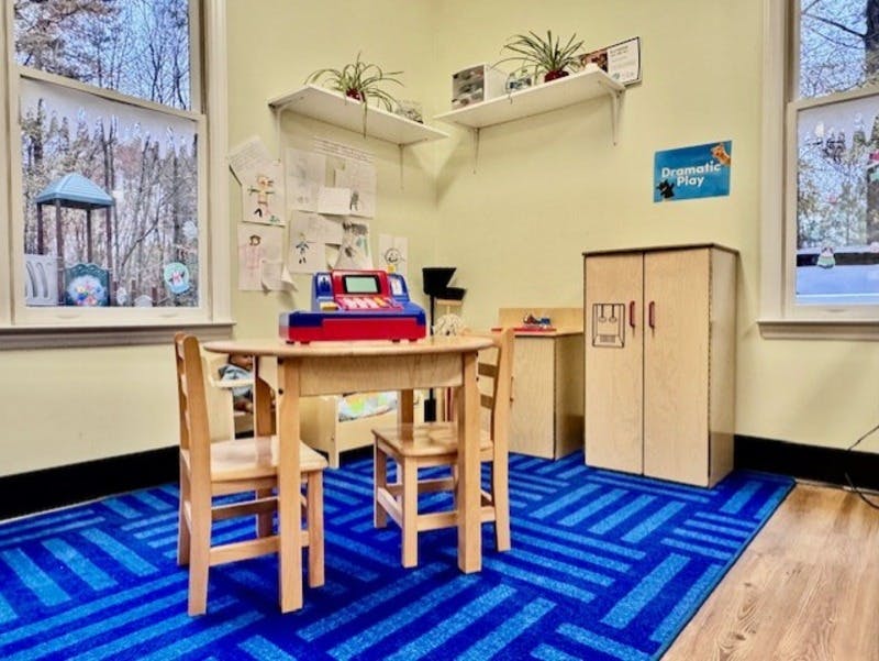 Children's dramatic play area with small table, chairs, and toy register
