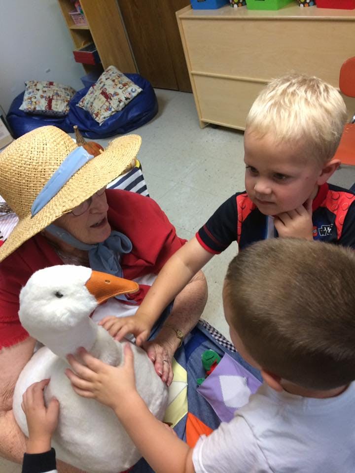 Person in straw hat with two children petting a stuffed goose