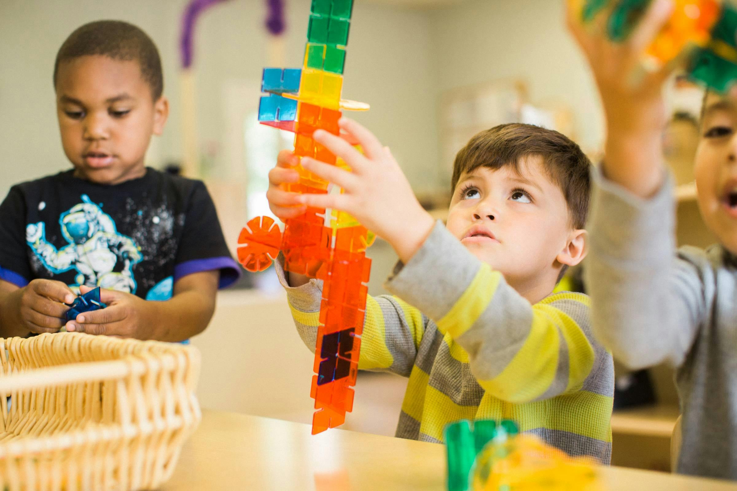 Child building with colorful blocks, another child holding a small toy