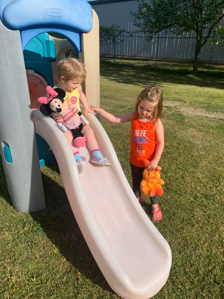 Child sitting on a slide with a Minnie Mouse doll, another child standing nearby