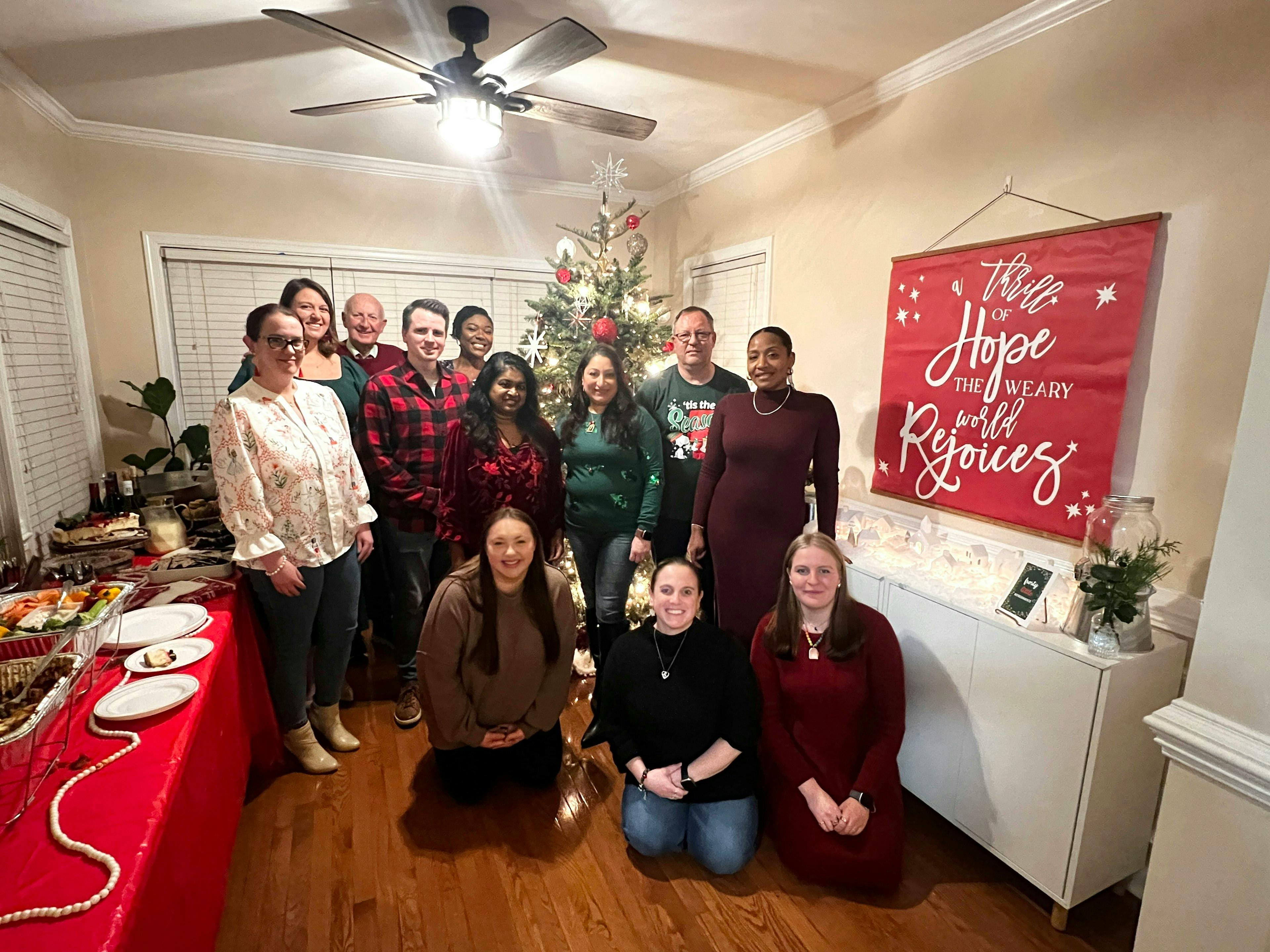 Group of adults posing for a photo in front of a Christmas tree and red banner