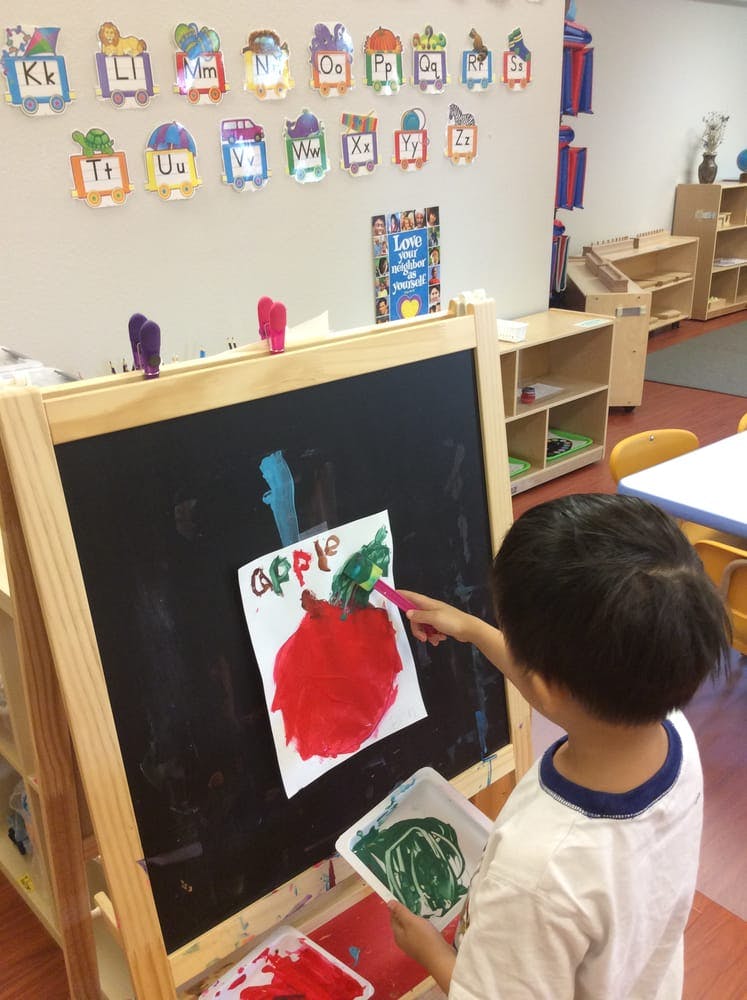 Child painting an apple on an easel in a classroom