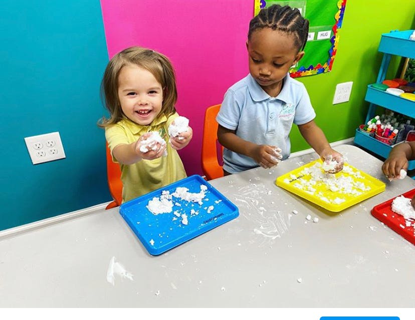 Two children playing with white dough on trays at a table