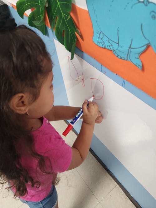 Child drawing on a whiteboard with a red marker