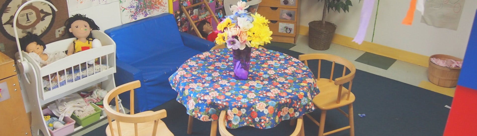 Dolls in a crib next to a table with a floral tablecloth and chairs