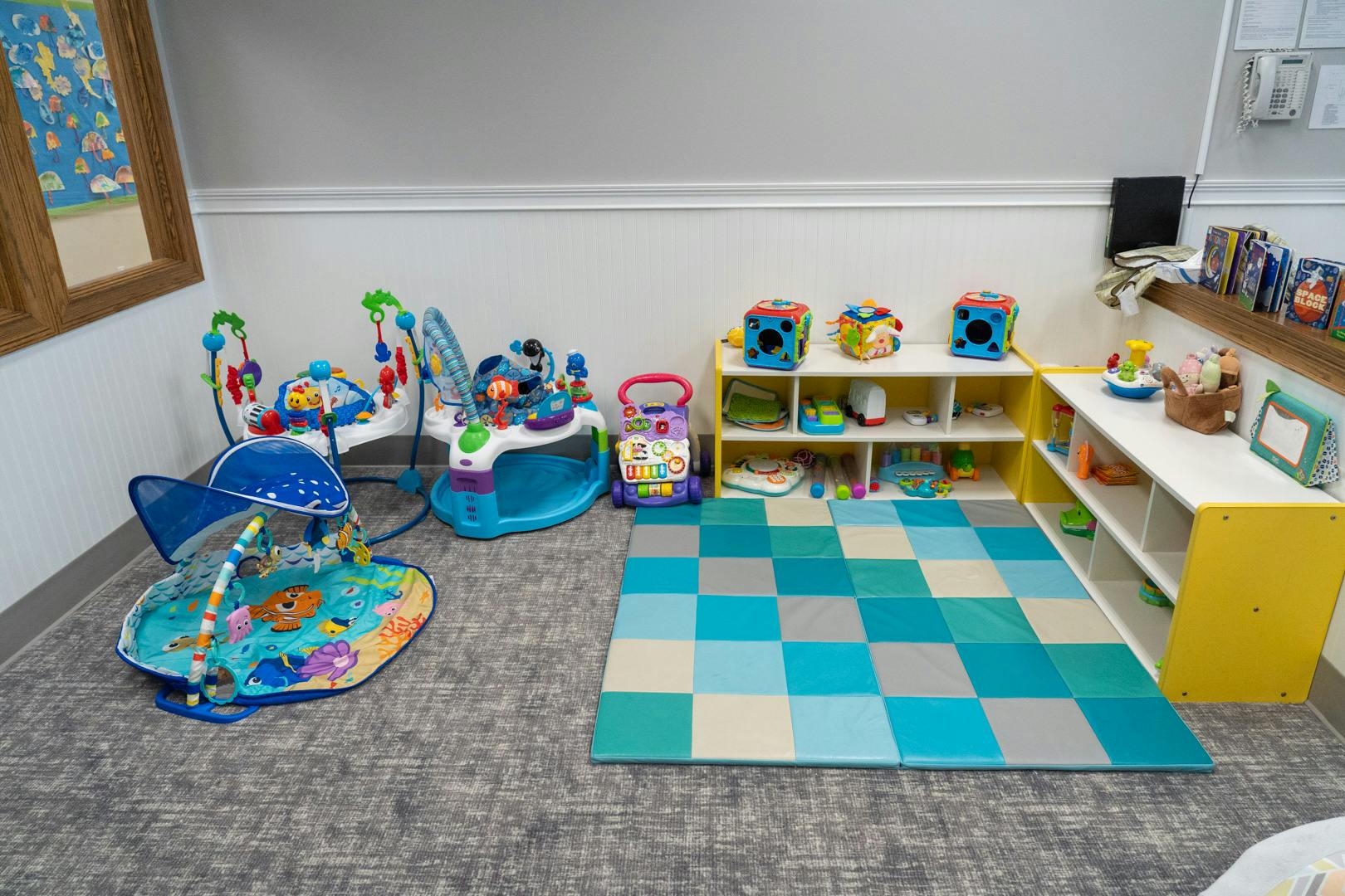 Playroom with baby activity centers, play mat, and shelves with toys
