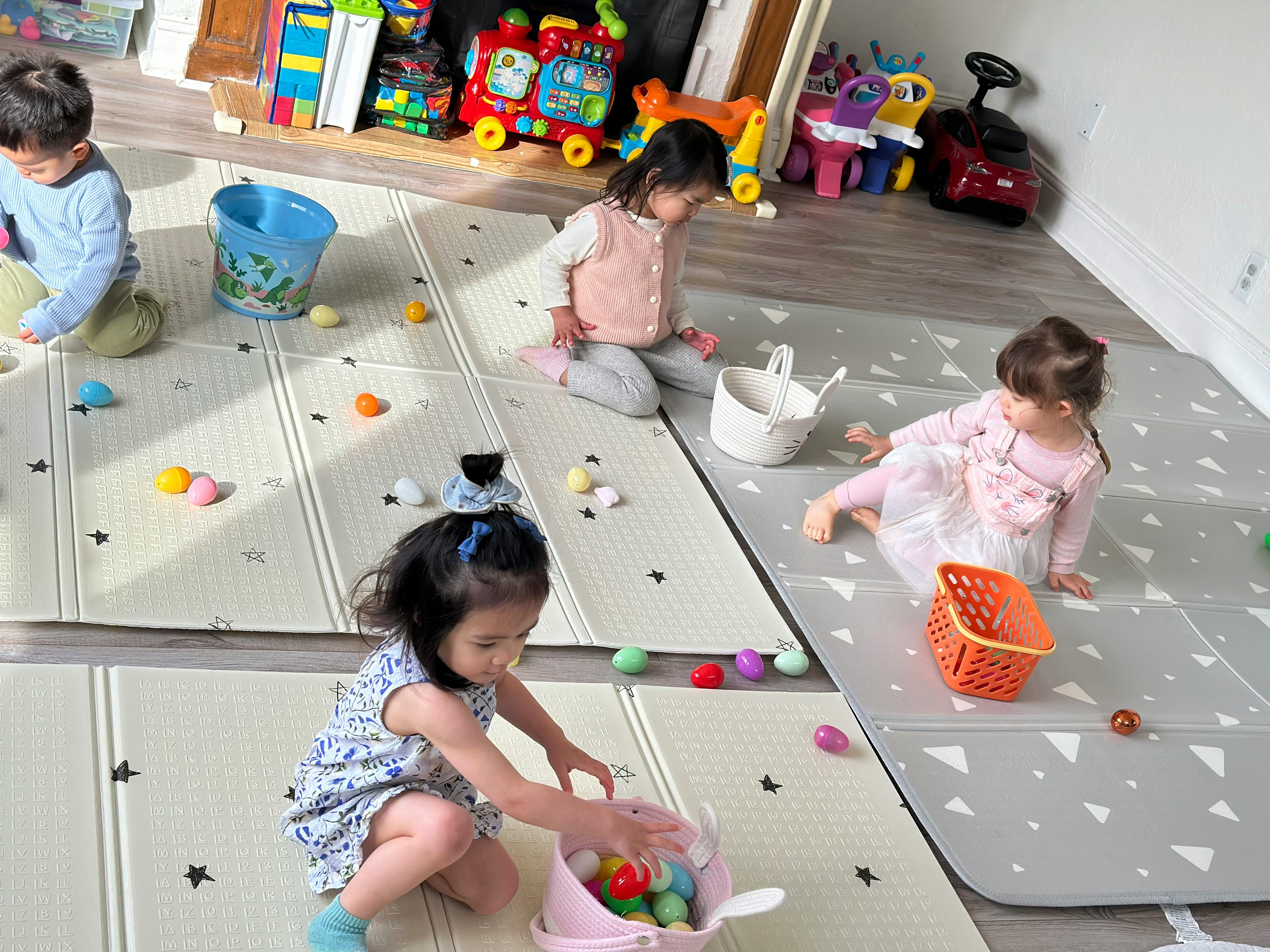 Four children playing with colorful plastic eggs and baskets on a play mat