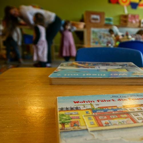 Children's books on a table with blurred adults and children in the background