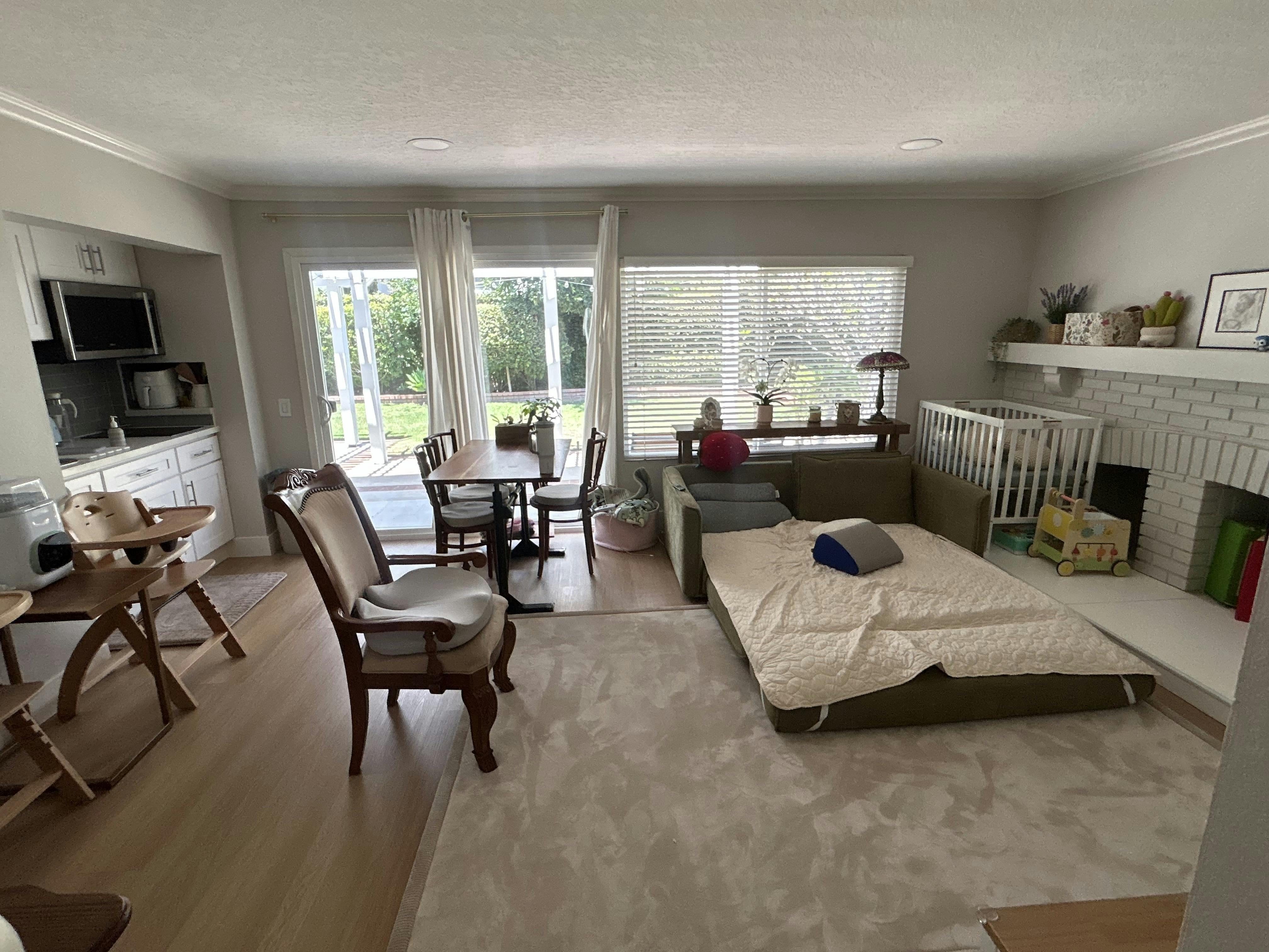 Living room with a sofa bed, dining table, kitchen, and a crib by the fireplace