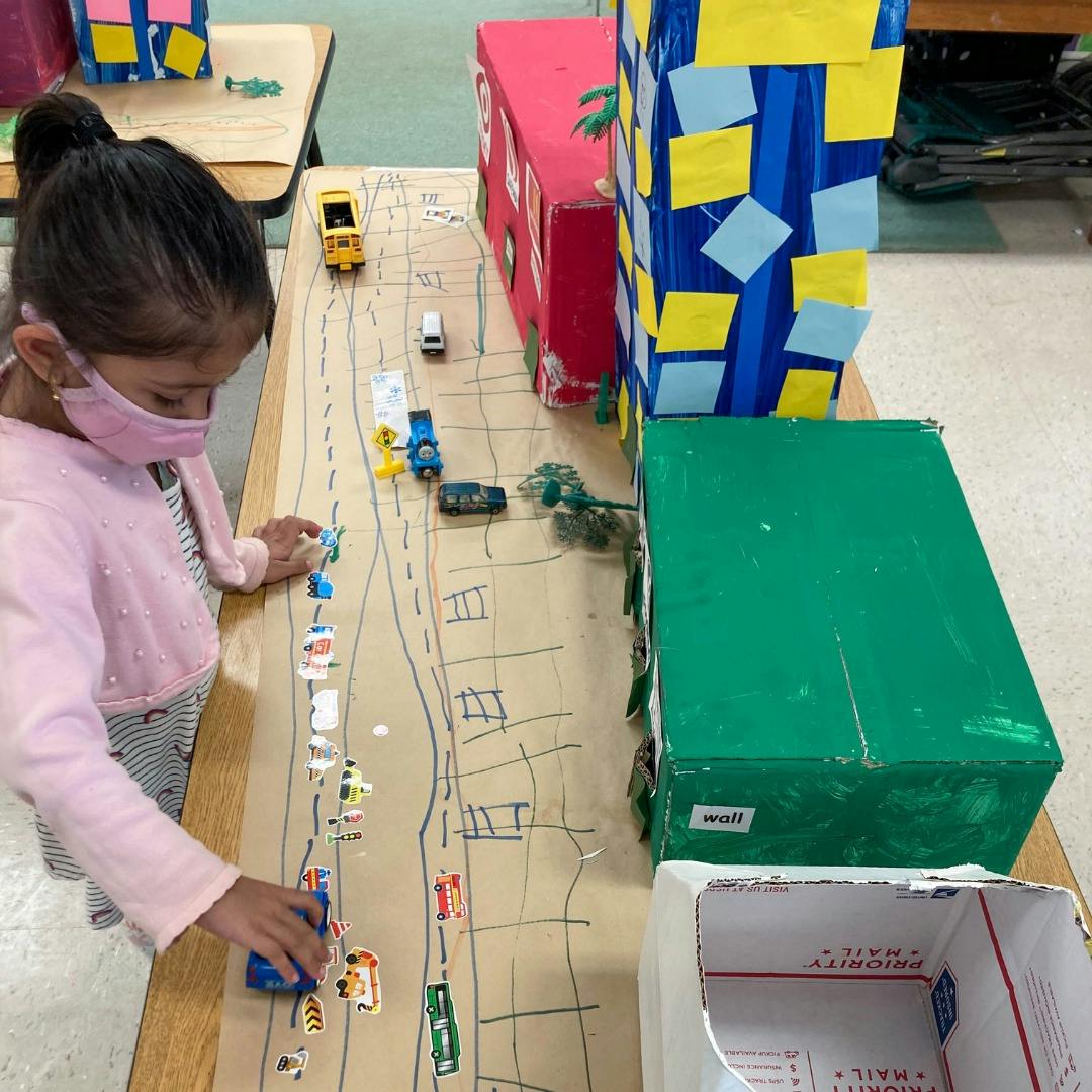 Child playing with toy cars on a drawn road with cardboard buildings
