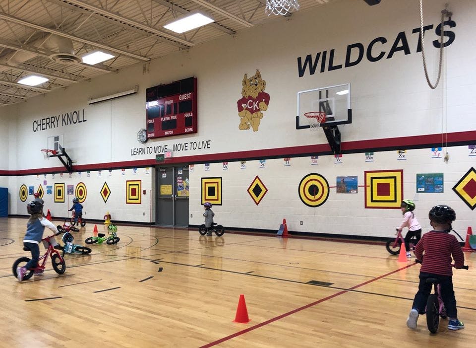 Children riding balance bikes in a gymnasium