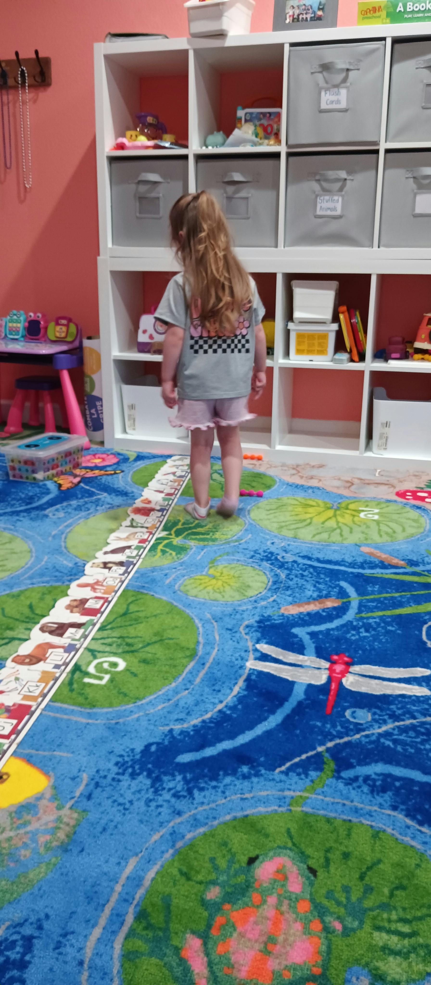 Child standing on a colorful rug in front of a storage shelf