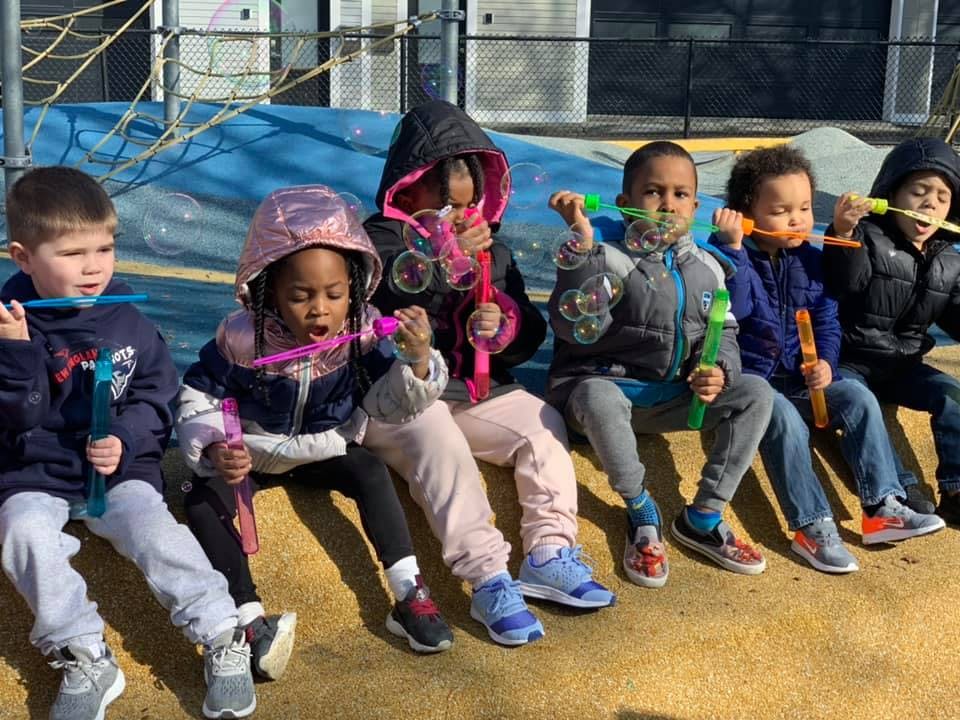Six children sitting in a row blowing bubbles