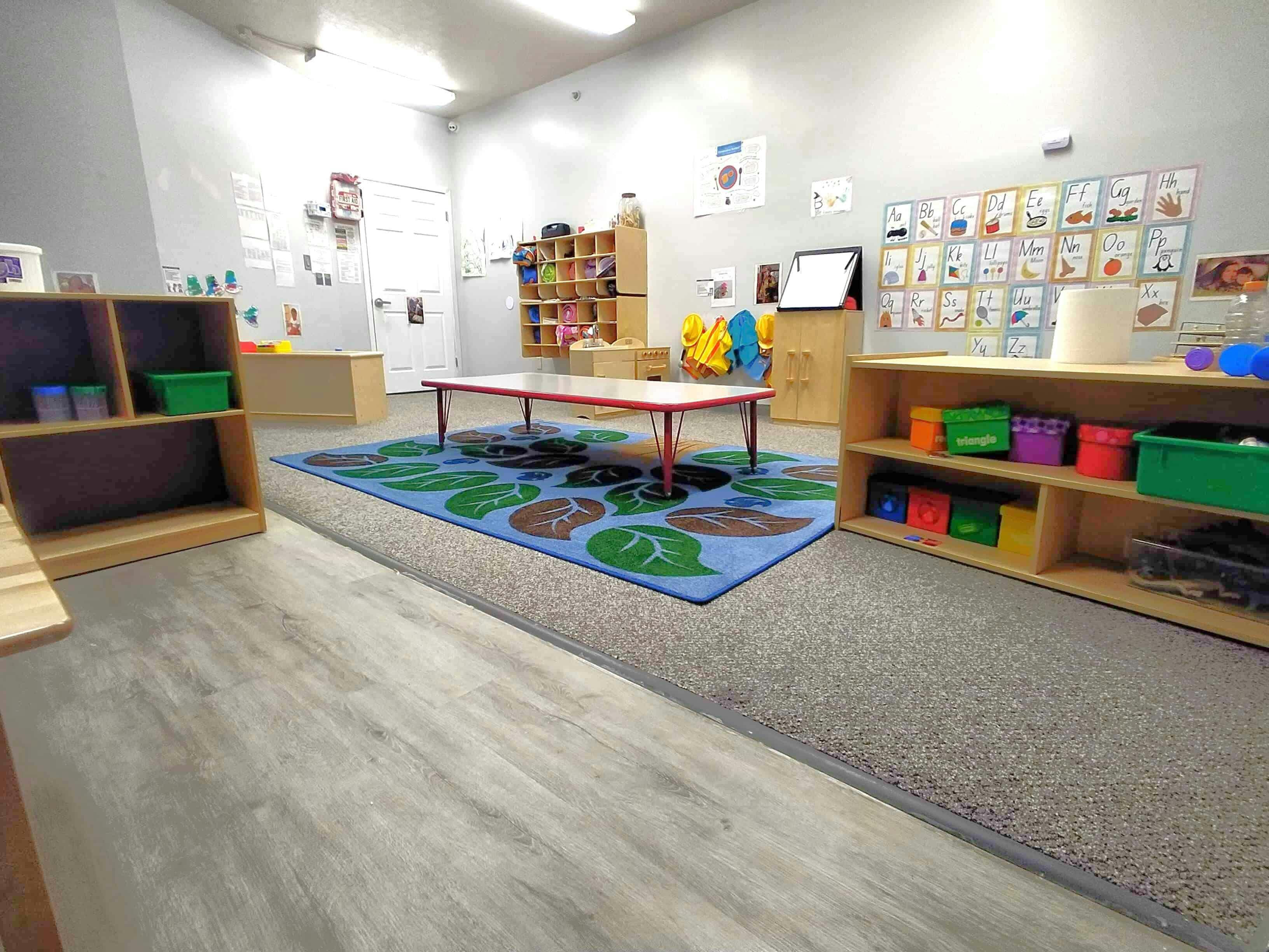 Classroom with small table on a blue rug and shelves with colorful bins