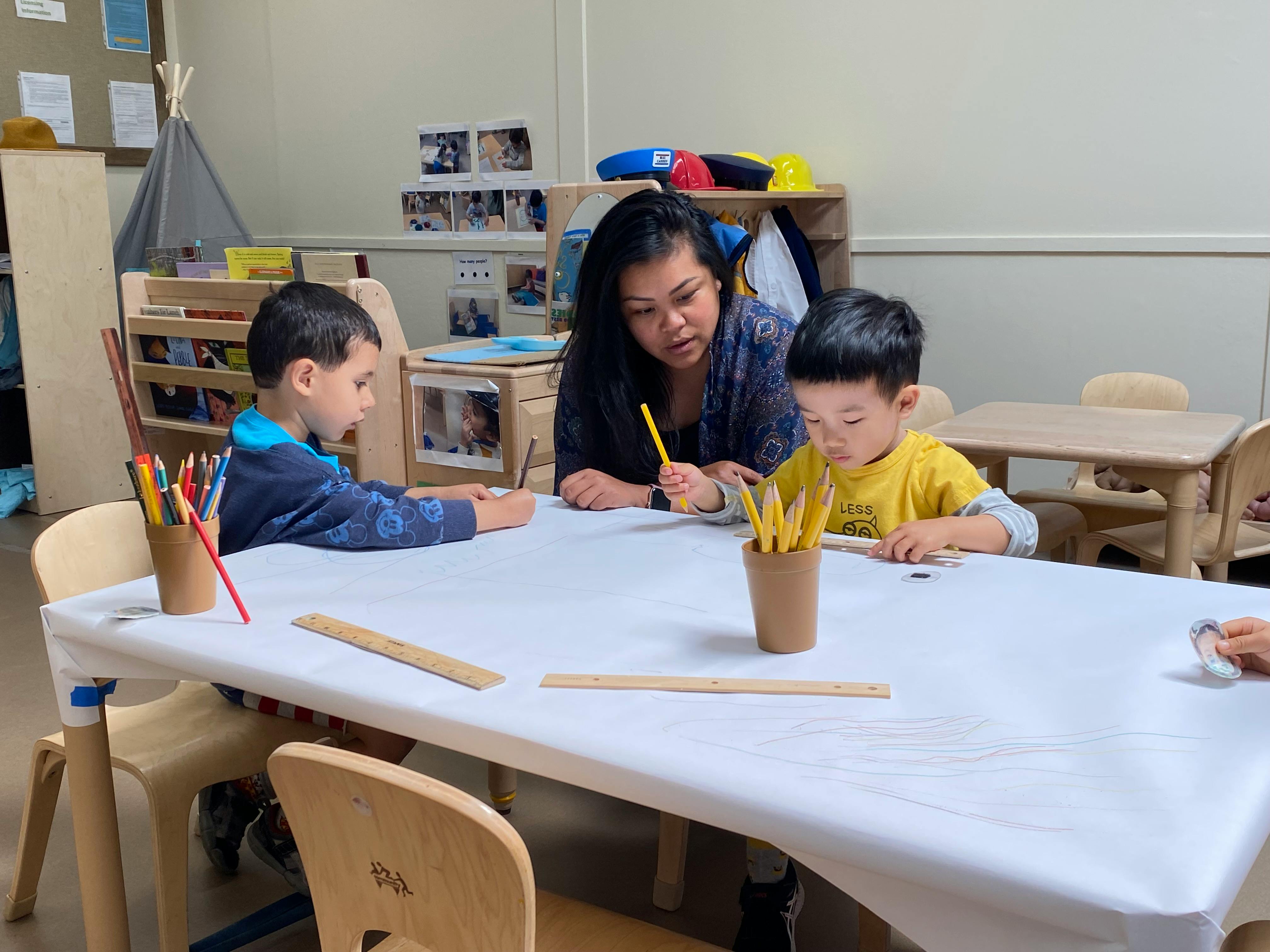 Adult and two children drawing at a table in a classroom