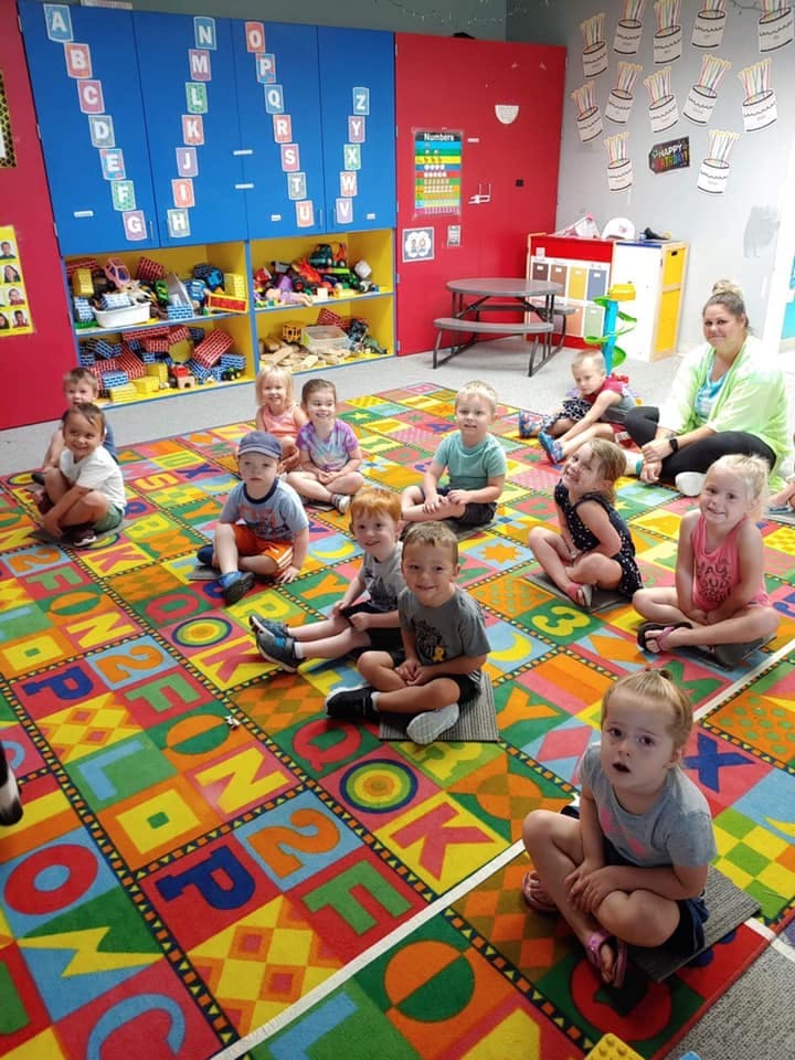 Children and an adult sitting on a colorful alphabet rug in a classroom