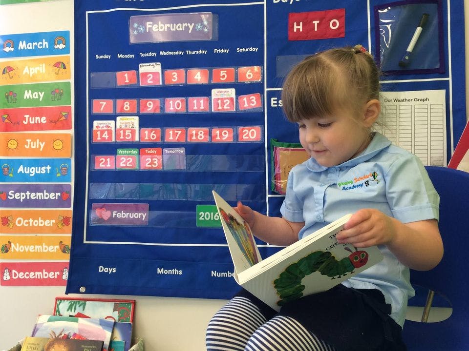 Child reading a book in a classroom with a calendar in the background