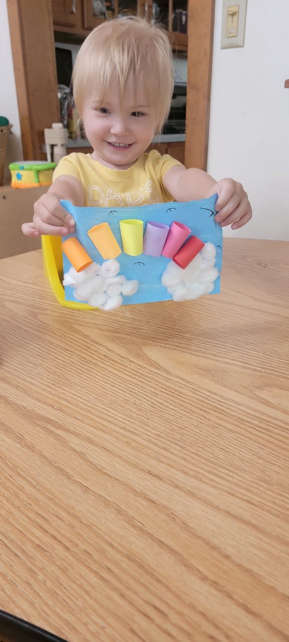 Child holding a craft project with colorful paper tubes and cotton balls