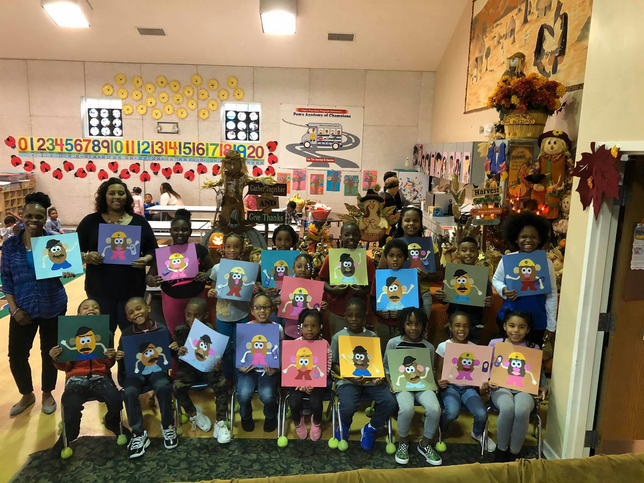 Adults and children holding up colorful drawings in a classroom