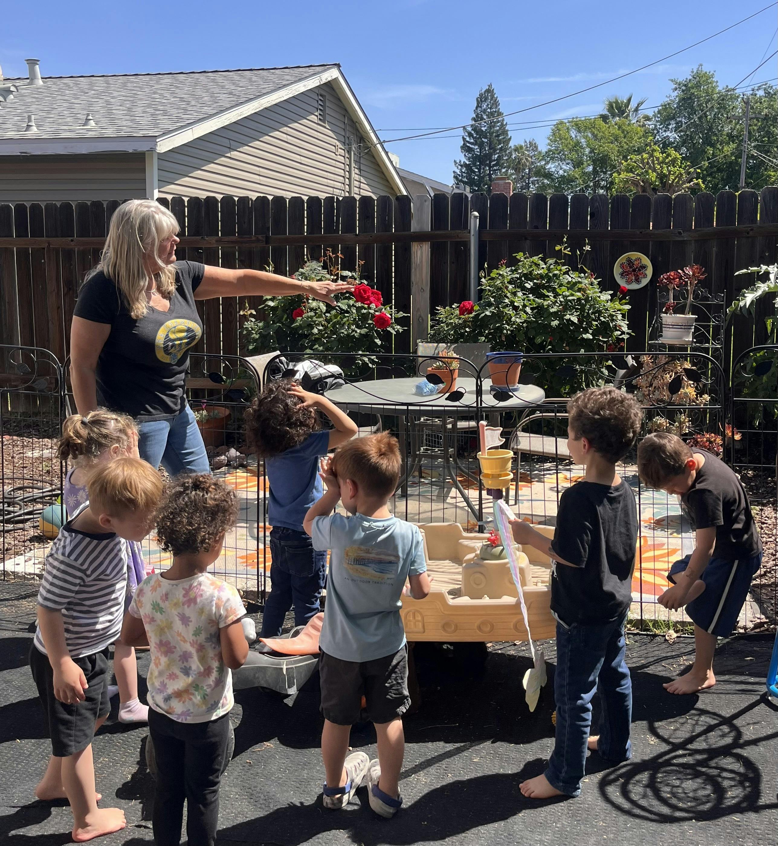 Adult pointing toward garden as children gather around a plastic boat play set