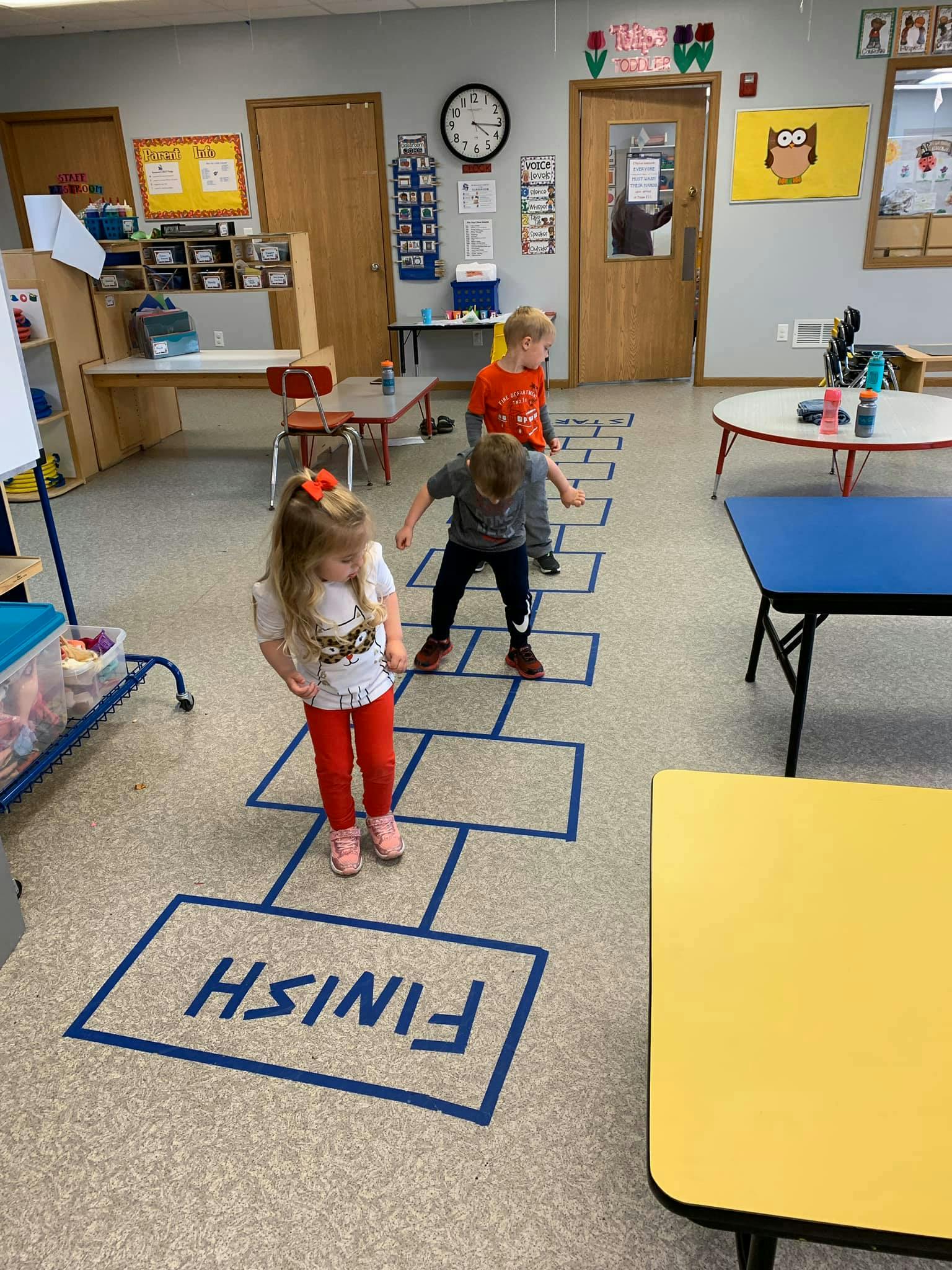 Three children playing hopscotch in a classroom