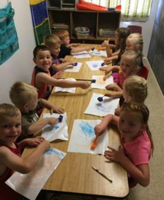 Children painting at a table in a classroom