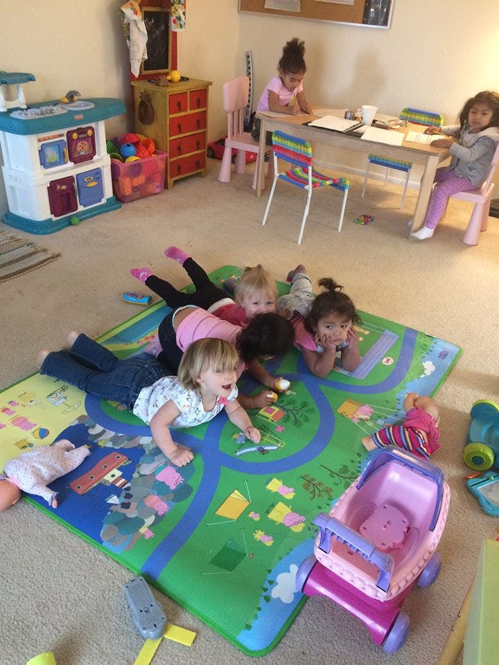 Children playing on a mat on the floor, others at a table