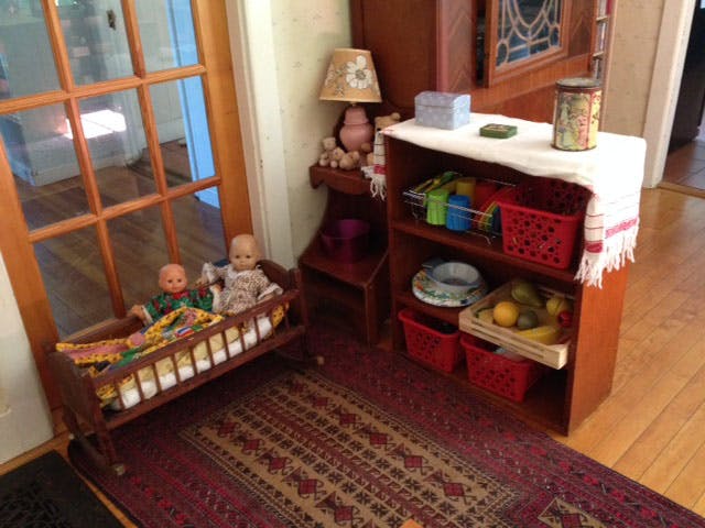 Two dolls in a wooden cradle next to a shelf with baskets and fruit