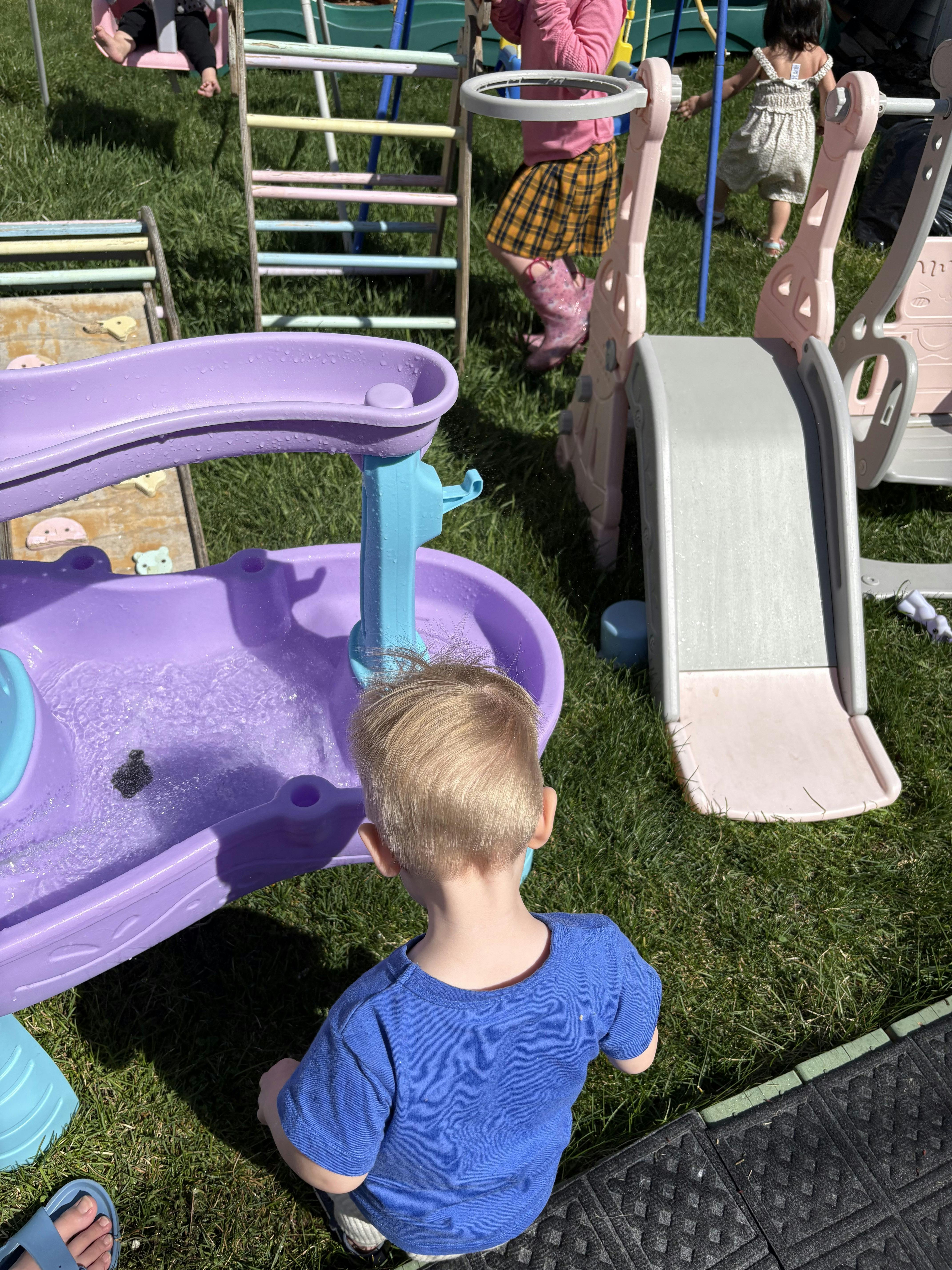 Child in blue shirt playing with a purple water table in grass