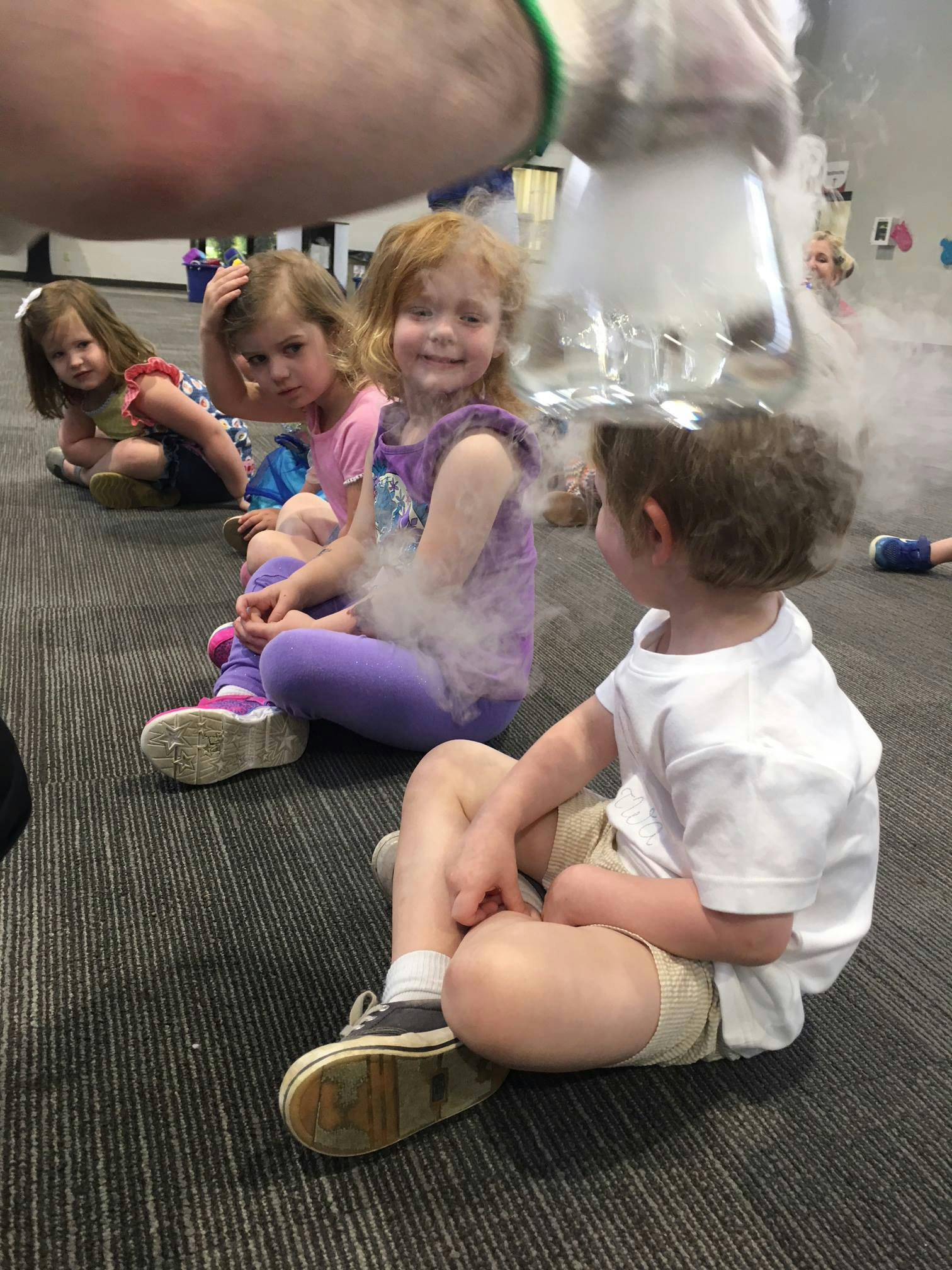 Children sitting on a floor watching a science demonstration with smoke