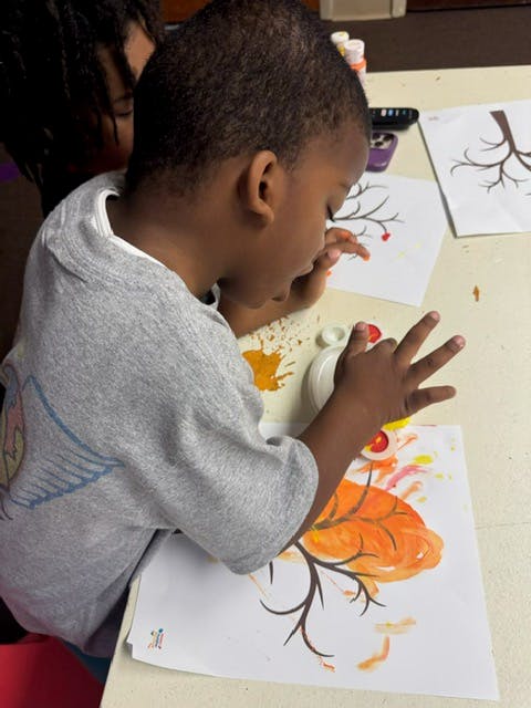 Child finger painting a tree with orange and yellow leaves