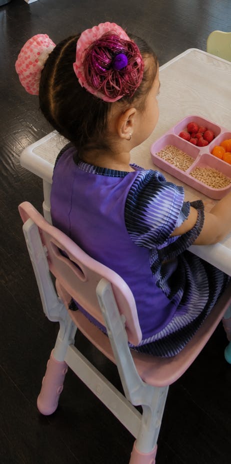Child sitting in a small chair at a table eating from a divided tray