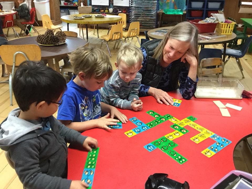 Adult and three children playing with colorful dominoes on a red table