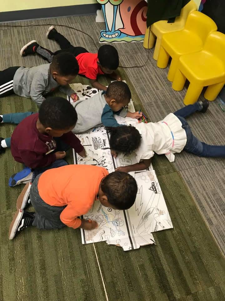 Children lying on the floor coloring on large sheets of paper