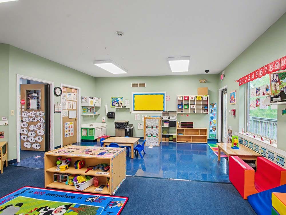 Empty kindergarten classroom with small tables, chairs, and shelves of toys