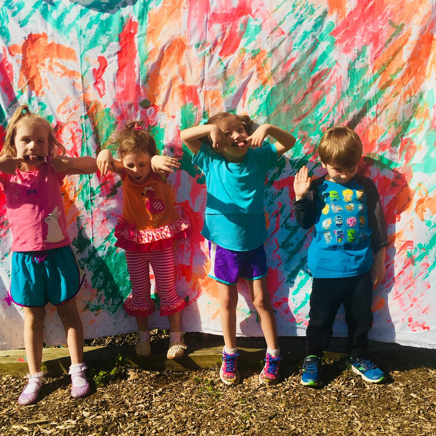 Four children making silly faces in front of a colorful painted backdrop