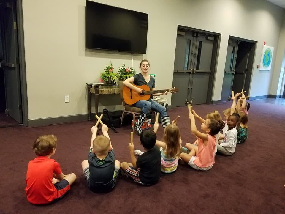 Person playing guitar for a group of children holding rhythm sticks