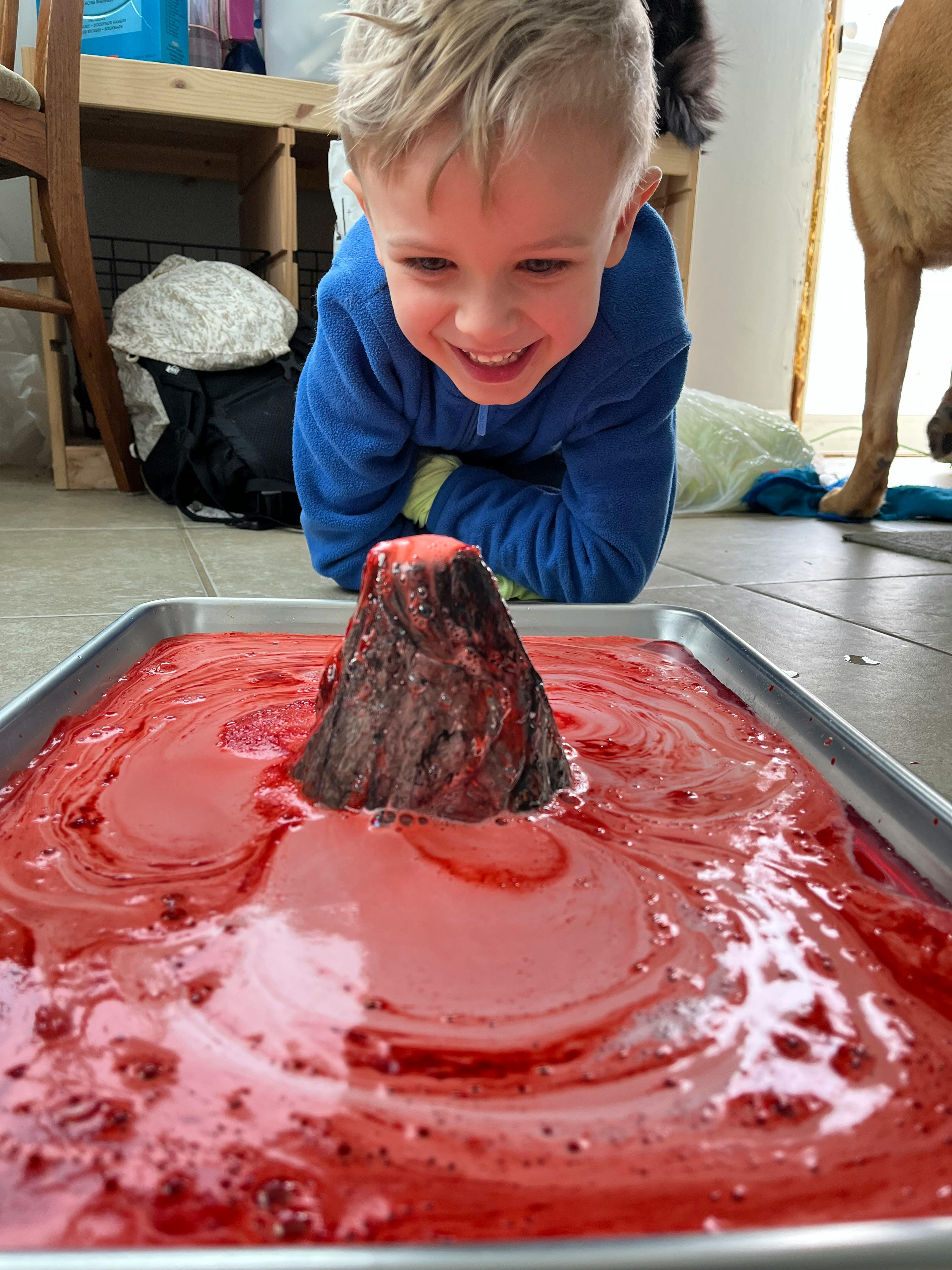 Child watching a volcano science experiment erupting red liquid
