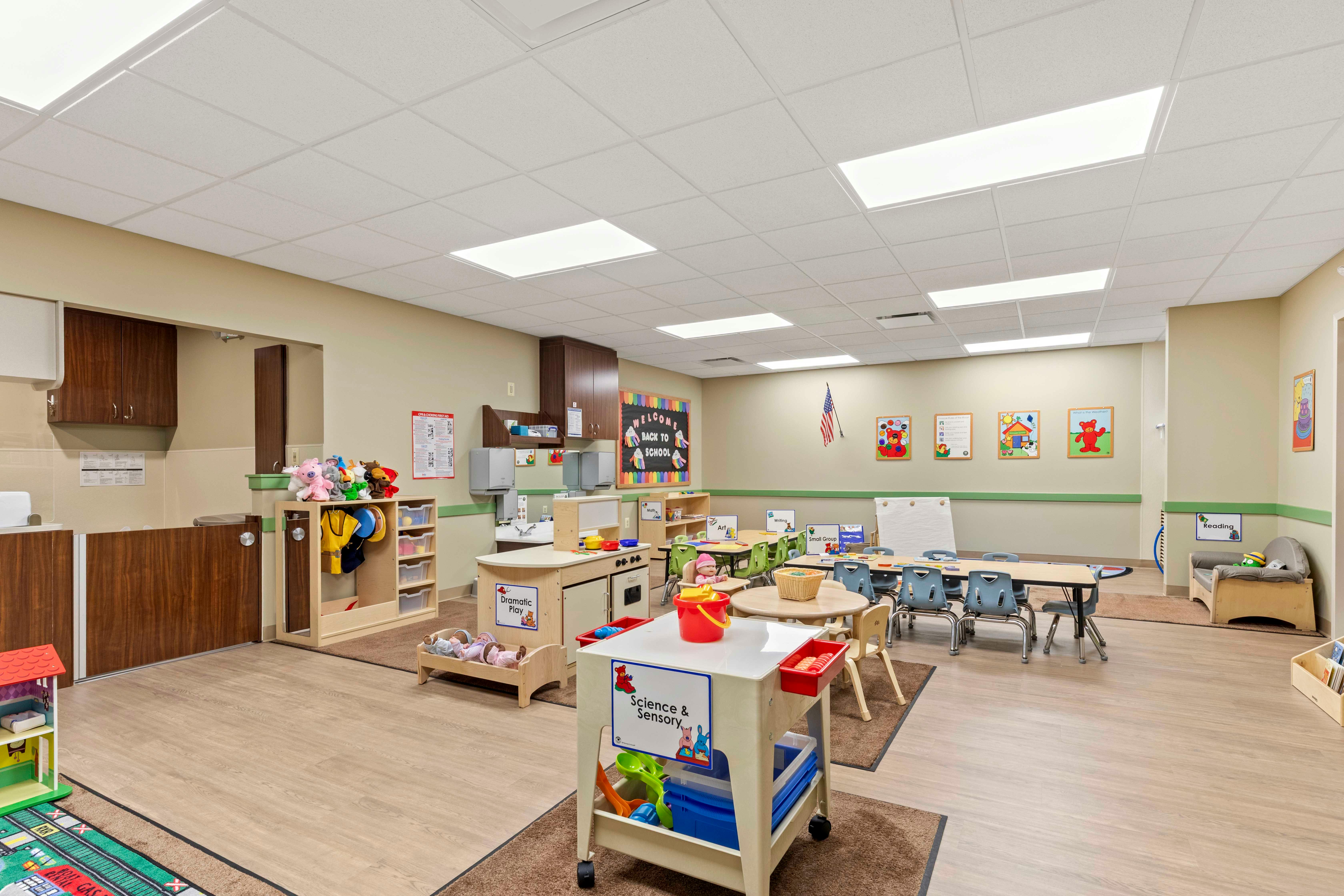 A colorful preschool classroom with various activity stations and small tables and chairs