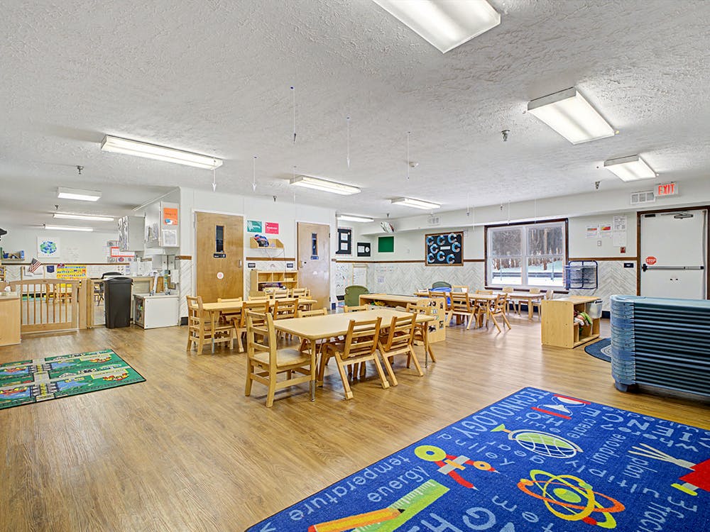 An empty classroom with tables, chairs, and colorful rugs on the floor