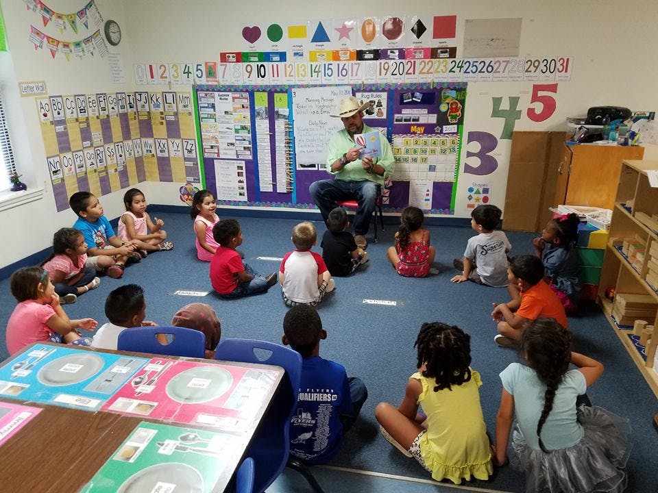 Adult reading to a group of children sitting on the floor in a classroom