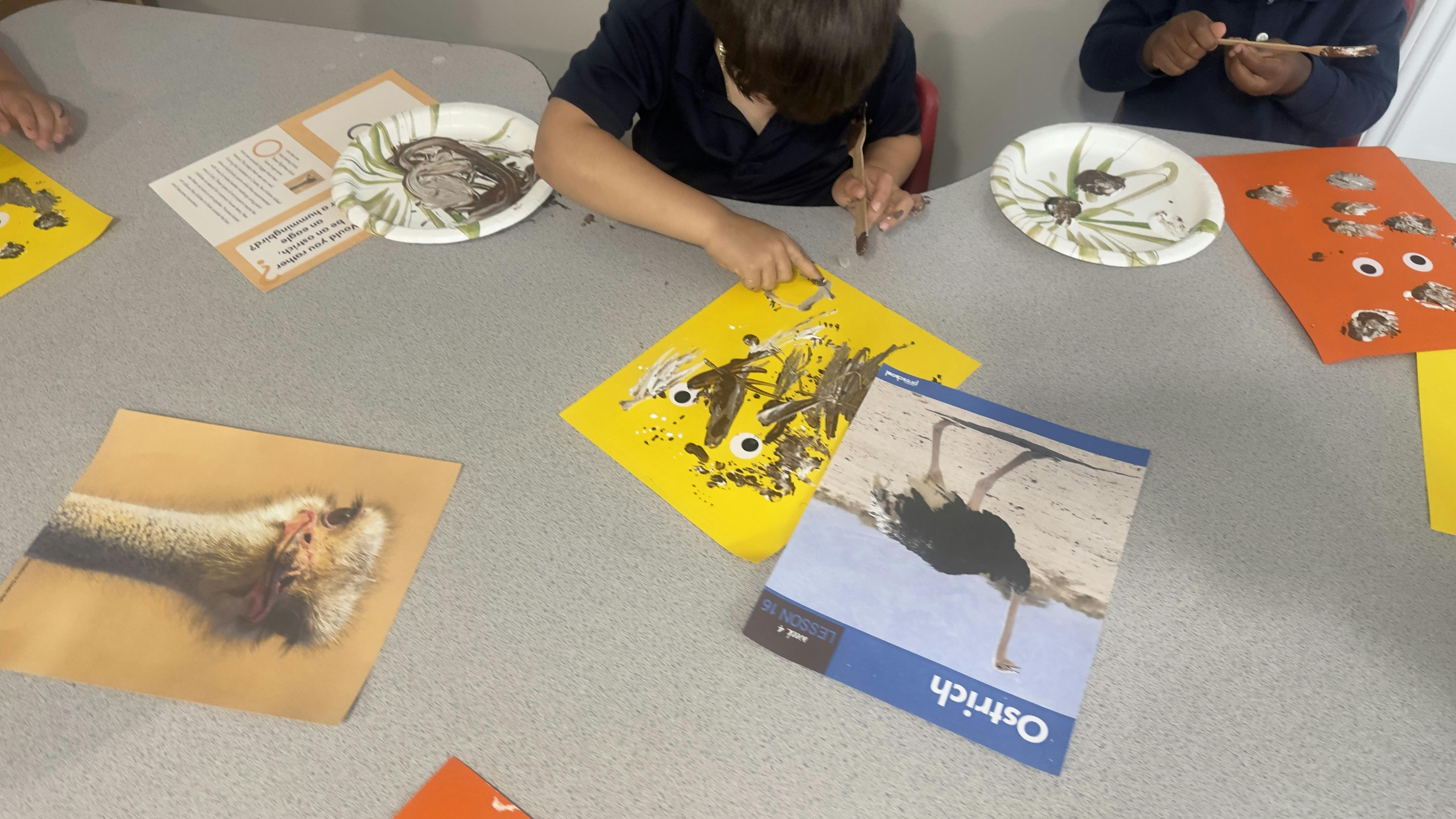Children painting with brown and white paint on colored paper with googly eyes