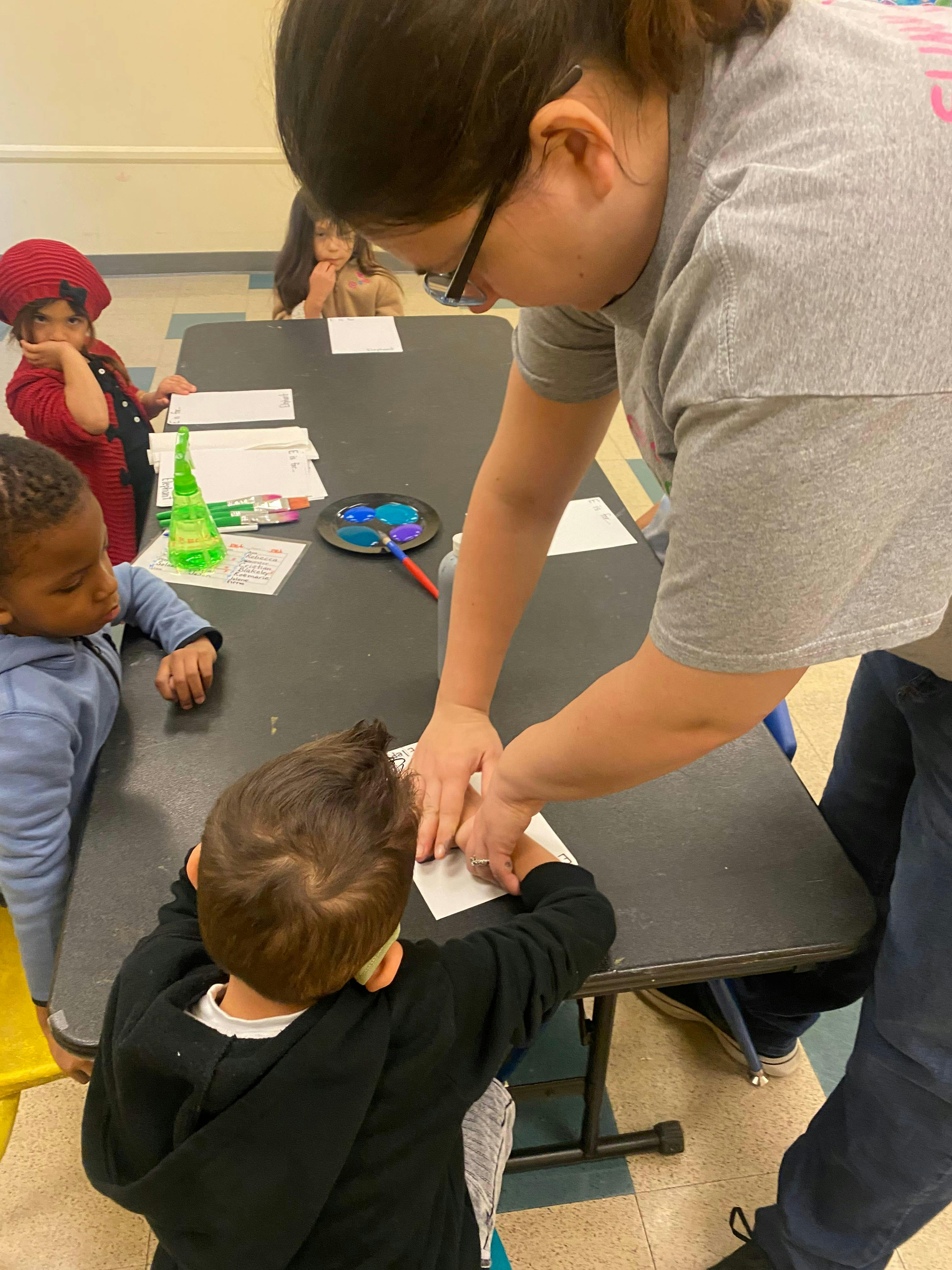 Person helping a child with an activity at a table in a classroom