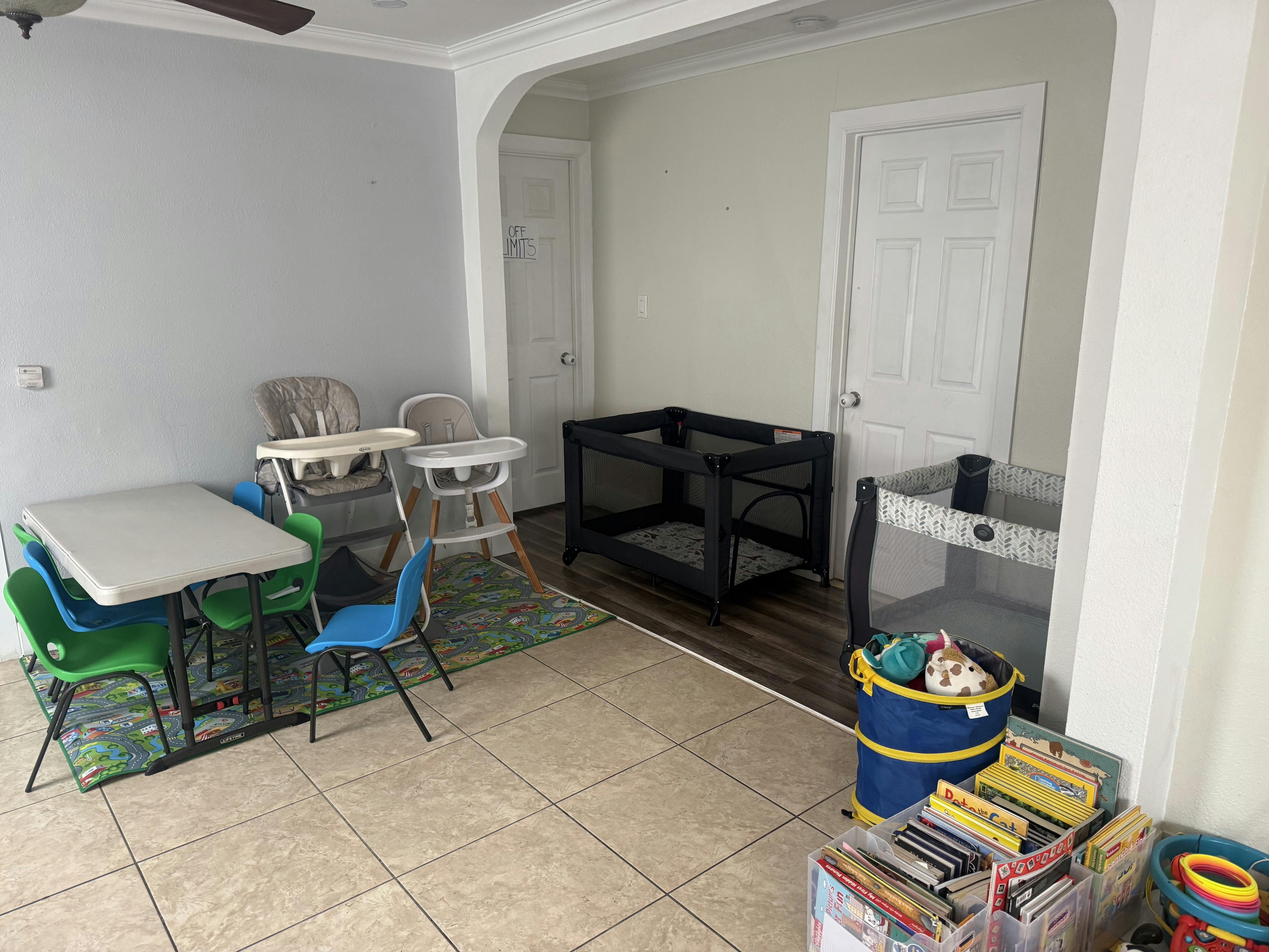 Children's play area with a table, chairs, high chairs, and two playpens